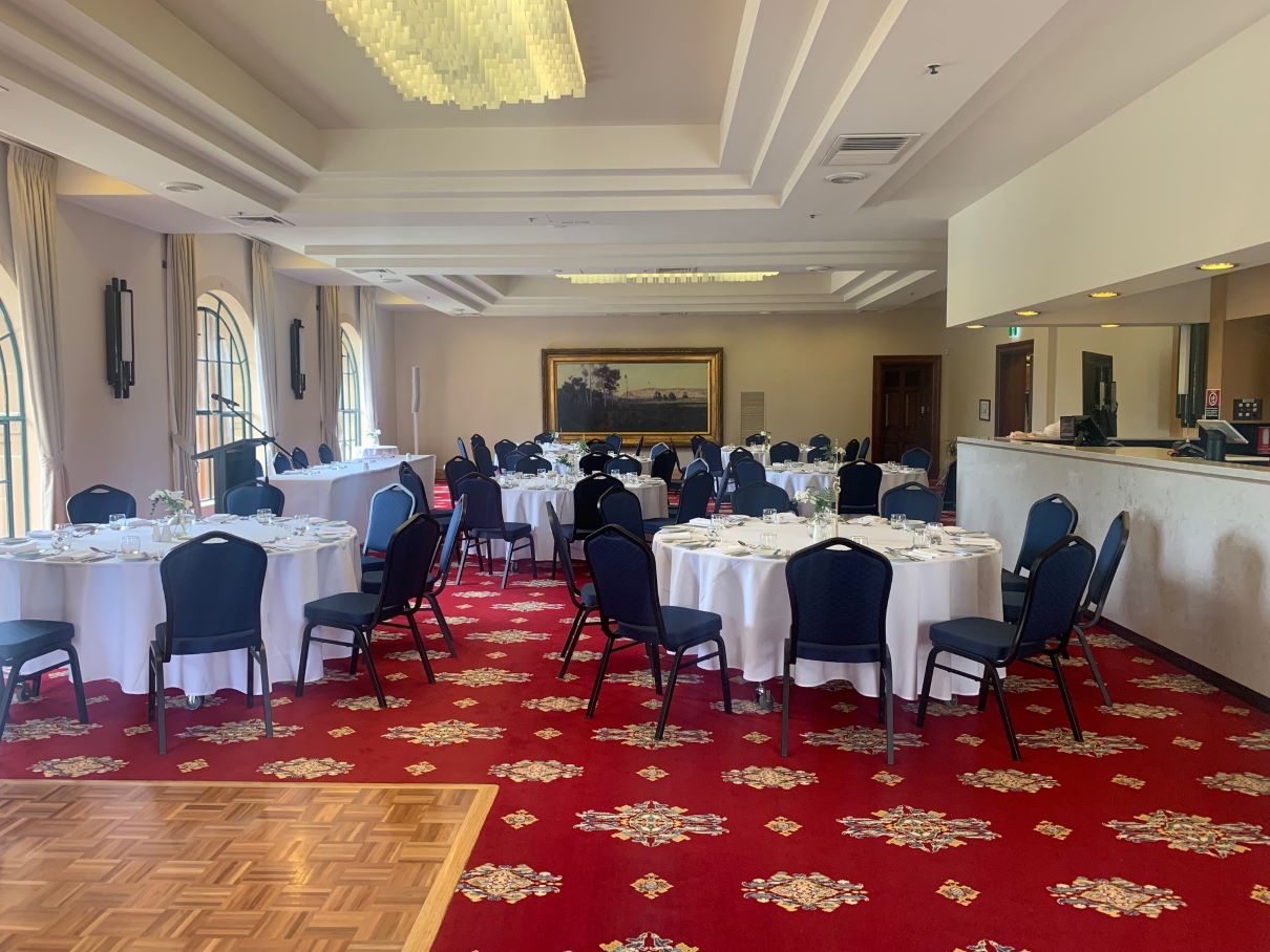 Hunter Room at Newcastle City Hall set up for a social event with round tables with white tablecloths and blue chairs.