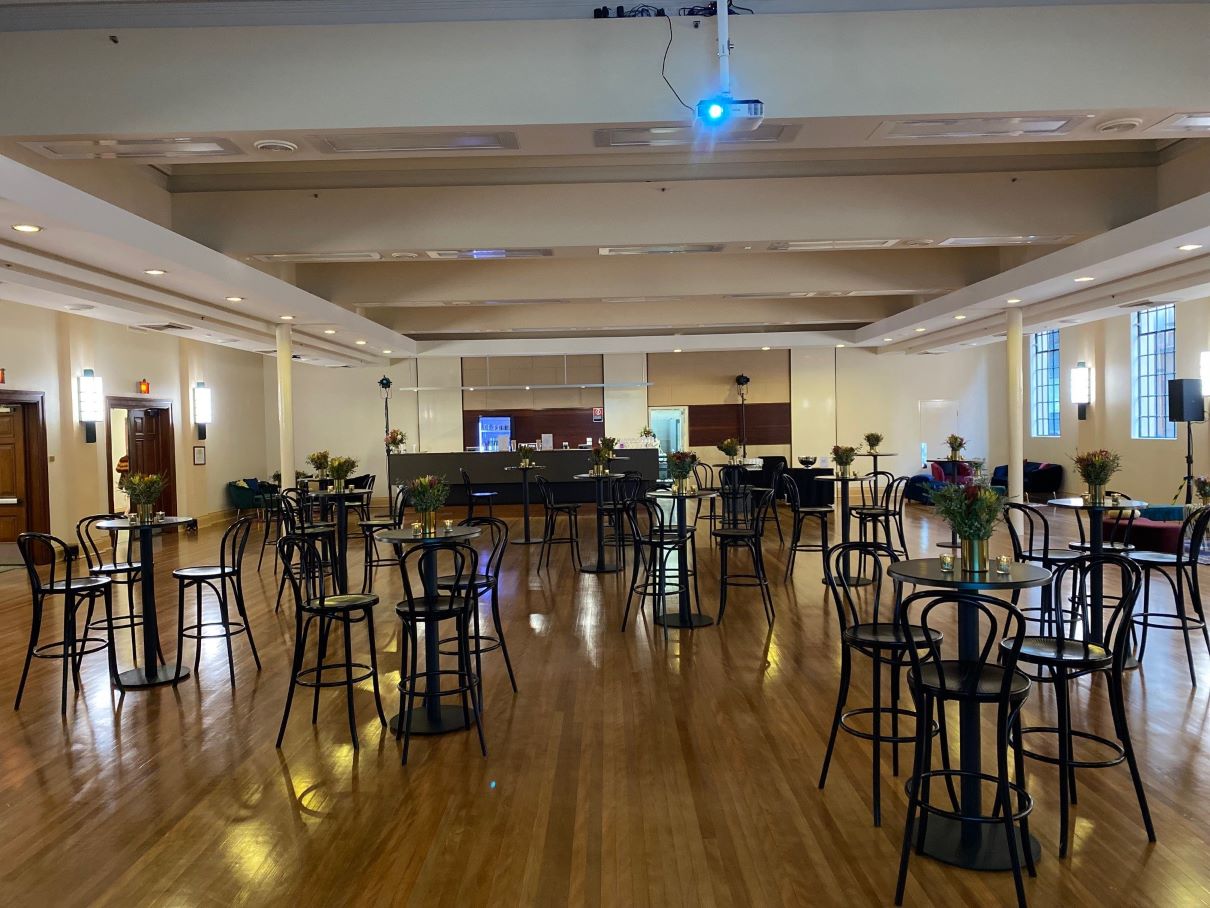 The Banquet Room at Newcastle City Hall set up for a social event with black high bar tables and chairs adorned with floral arrangements, spread out across the polished floors of the room.